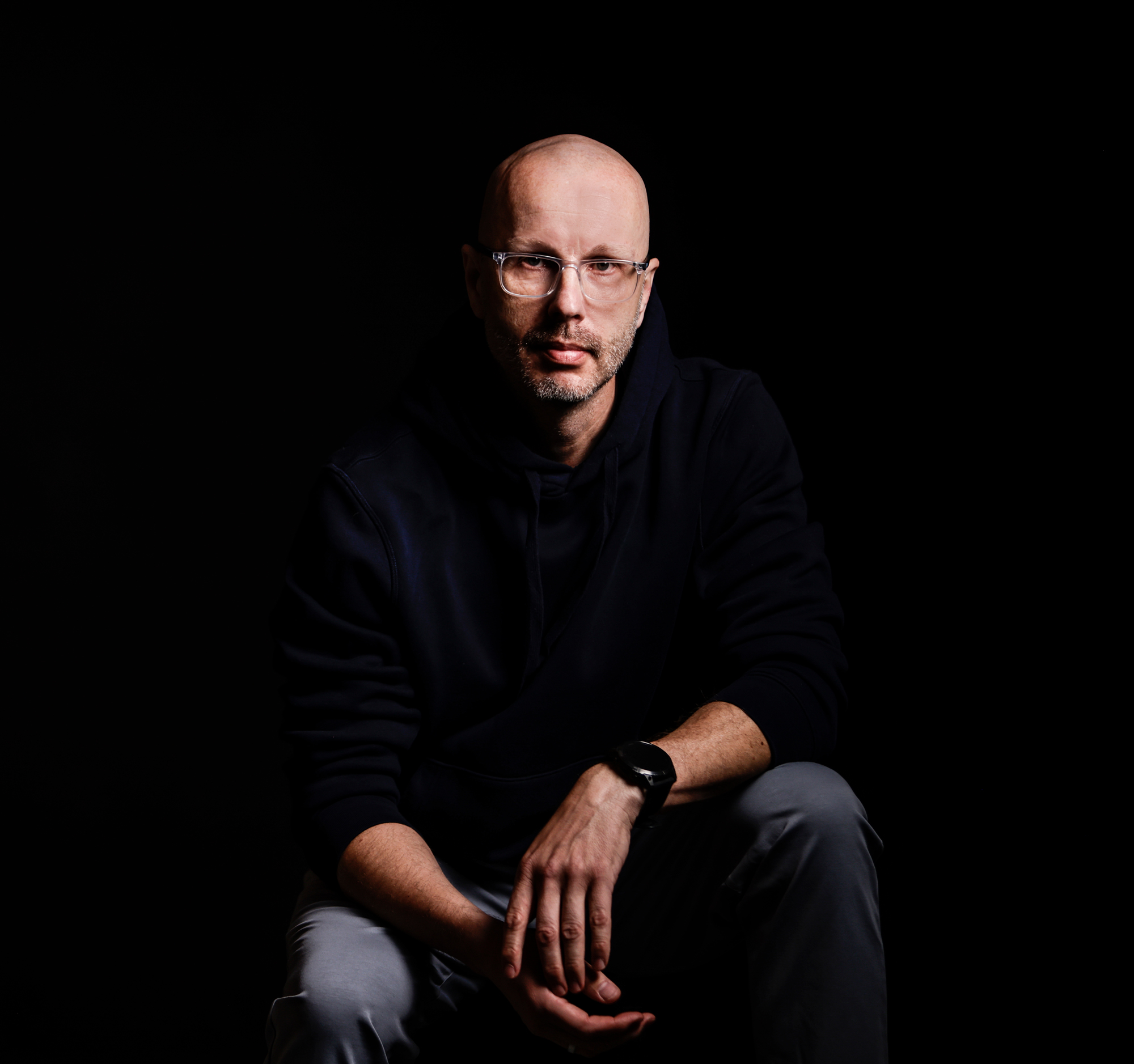 Foto von Axel Hillebrandt im dunklen Hoodie vor schwarzem Hintergrund, sitzend und nach vorne gelehnt.